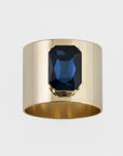 A gold-colored napkin ring with a navy blue gemstone centerpiece.