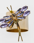A gold-colored napkin ring adorned with purple amethyst and topaz glass crystals designed to resemble a dragonfly.