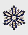 A navy and crystal brooch shaped like a starburst with a central large crystal, surrounded by smaller crystal accents and navy blue enamel.