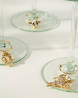 Gold wine glass charms with decorative elements on a white surface