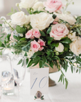 Floral arrangement with pink and white roses on a table with a table number card.