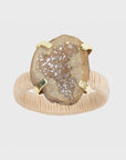 A napkin ring featuring a natural raffia band and a druzy stone centerpiece, with a gold-colored metal clasp.