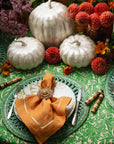 Decorative table setting with pumpkins, flowers, and green plates on a patterned tablecloth.