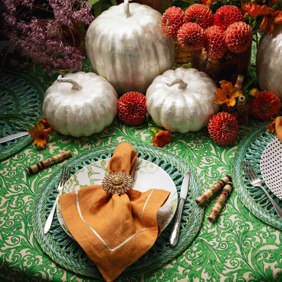 Decorative table setting with pumpkins, flowers, and green plates on a patterned tablecloth.