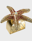 A gold-colored starfish-shaped napkin ring adorned with pink and clear embellishments.