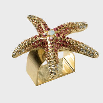 A gold-colored starfish-shaped napkin ring adorned with pink and clear embellishments.
