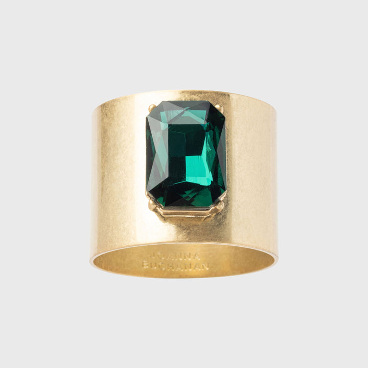 A gold-colored napkin ring featuring a large emerald-cut green gemstone.