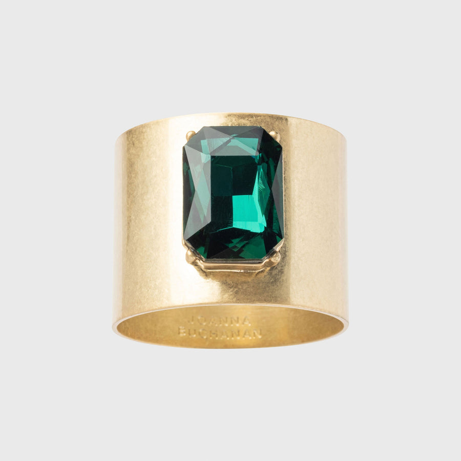 A gold-colored napkin ring featuring a large emerald-cut green gemstone.