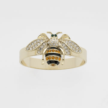 A gold-colored napkin ring featuring a skinny stripey bee design with black, white, and orange details.