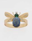 A gold-colored napkin ring featuring a lapis lazuli stone and intricate wing details, designed to resemble a bug.
