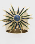 A gold-colored starburst napkin ring featuring a central lapis lazuli stone with blue and green gemstone accents.