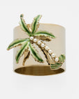 A gold-colored napkin ring featuring a hand enameled palm tree with green fronds and faux-pearl trunks.