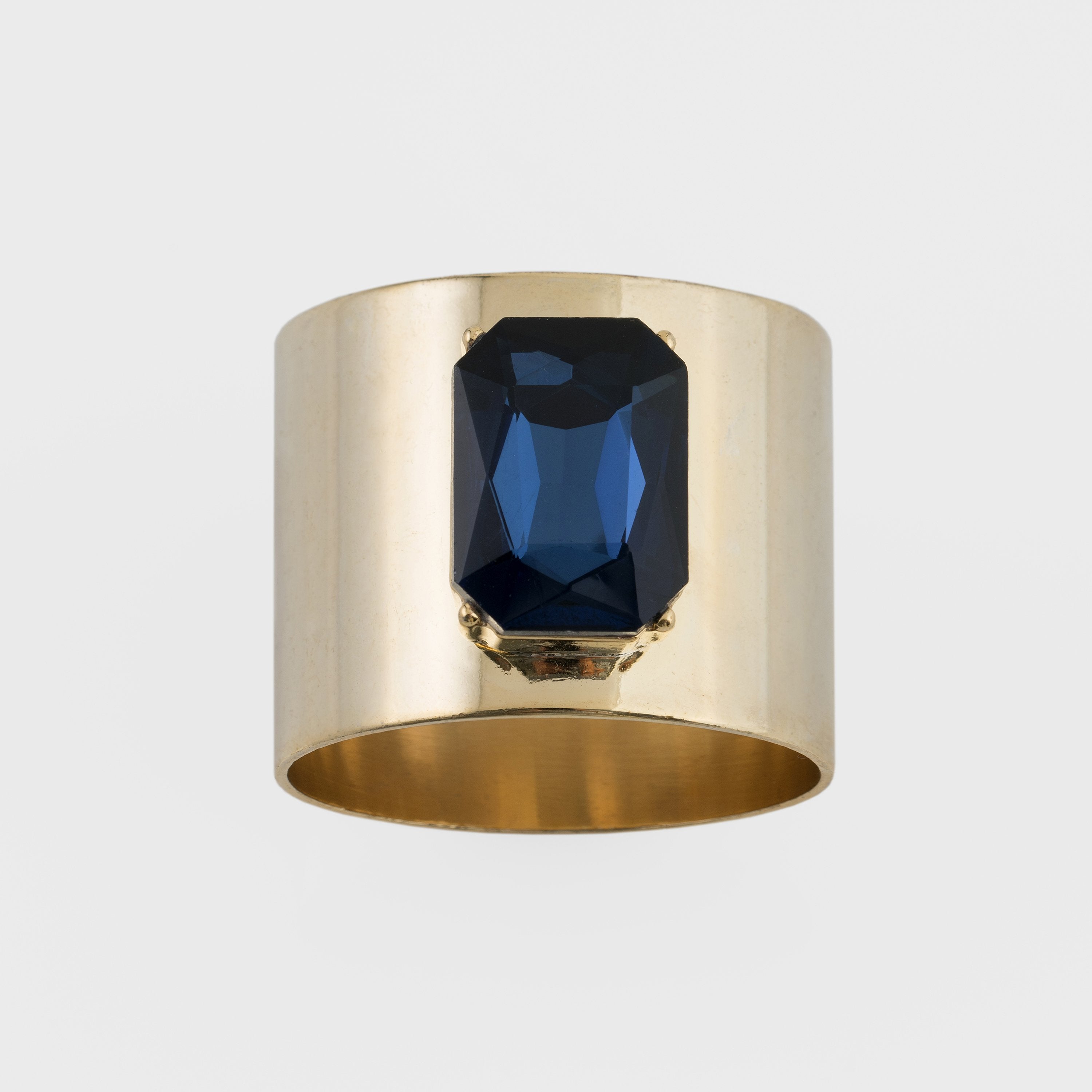 A gold-colored napkin ring with a navy blue gemstone centerpiece.