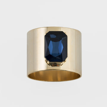 A gold-colored napkin ring with a navy blue gemstone centerpiece.