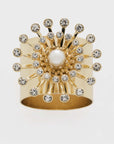 A gold-colored napkin ring featuring a faux pearl at the center with sparkling crystals radiating outward.