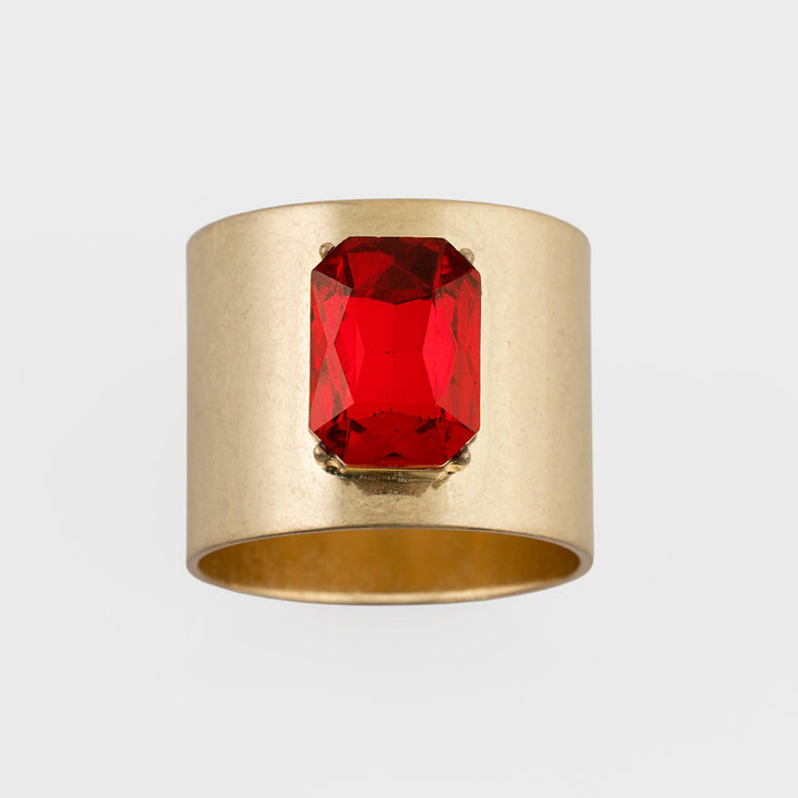 A gold-colored napkin ring with a bright red jewel in the center.