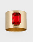 A gold-colored napkin ring with a bright red jewel in the center.
