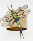 A gold-colored napkin ring featuring a dragonfly design with green and blue accents, and opal colored glass stones.