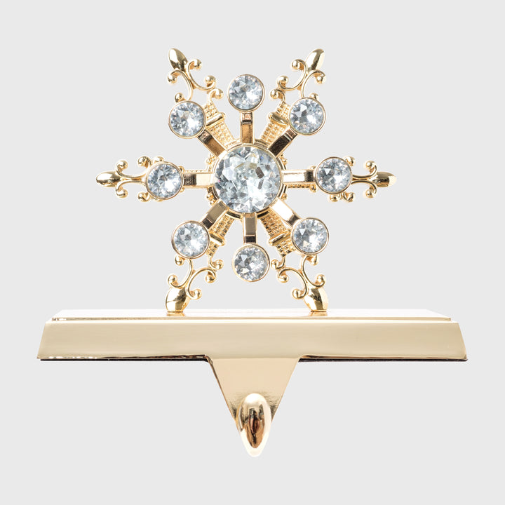 A gold-colored stocking hanger with a snowflake design embellished with clear crystals.