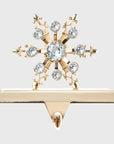 A gold-colored stocking hanger with a snowflake design embellished with clear crystals.