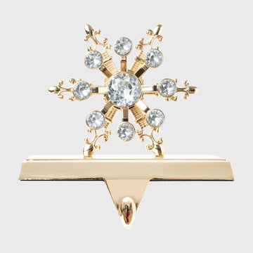 A gold-colored stocking hanger with a snowflake design embellished with clear crystals.