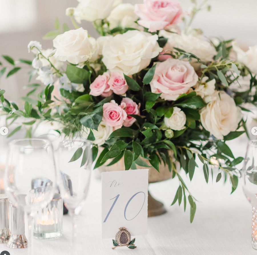 Floral arrangement with pink and white roses on a table with a table number card.
