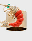 A shrimp-shaped napkin ring with a gold body, red coral, and diamond-like embellishments.