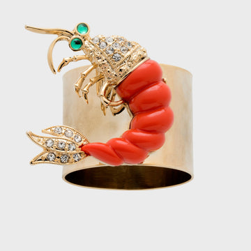 A shrimp-shaped napkin ring with a gold body, red coral, and diamond-like embellishments.