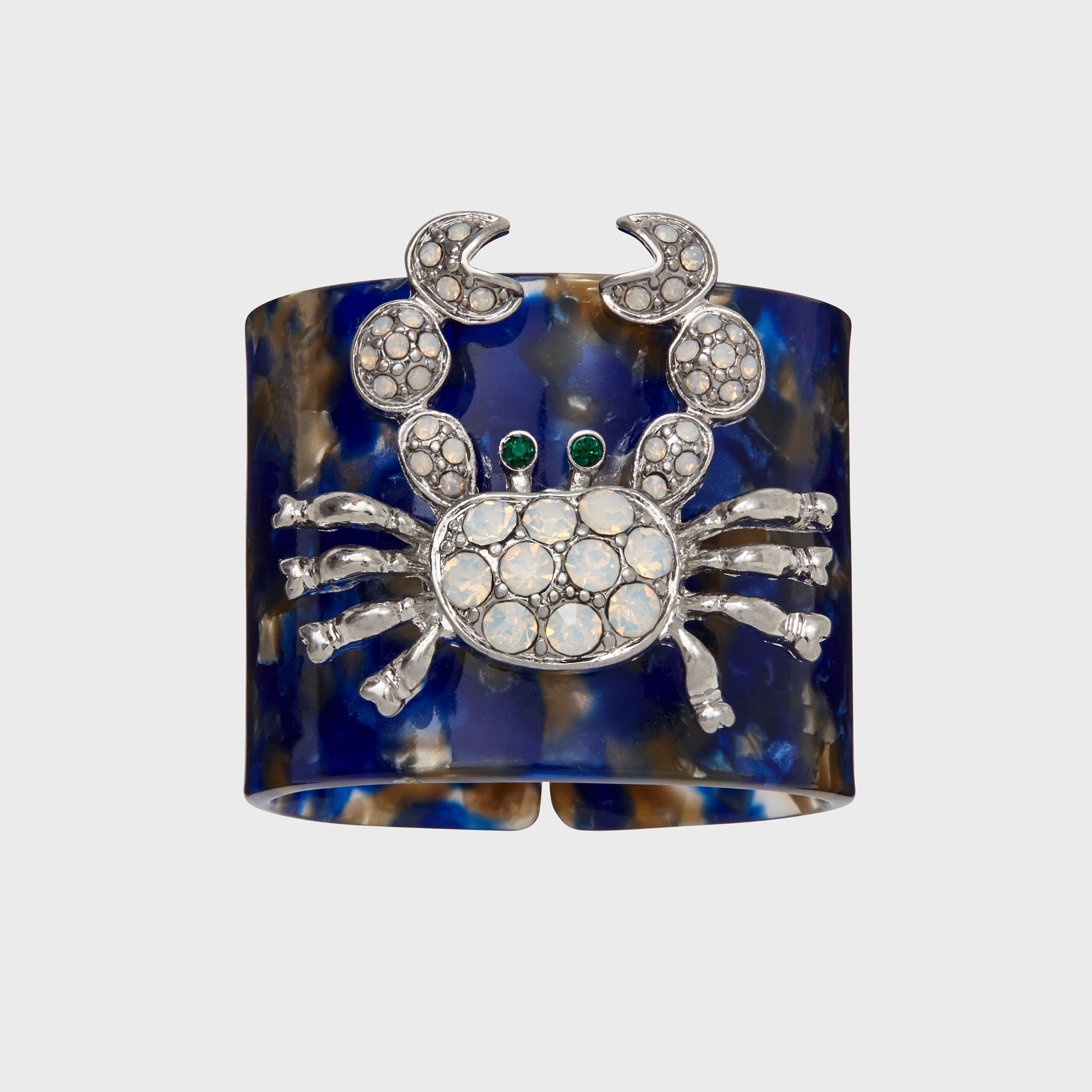 A blue and brown tortoiseshell resin napkin ring with a crab design in the center, adorned with sparkling embellishments.