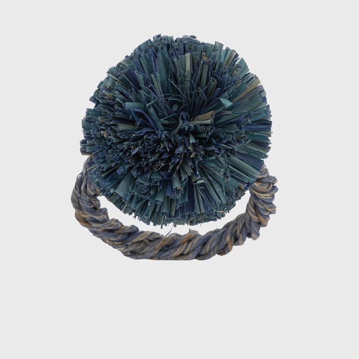 A straw pompom napkin ring in indigo blue color, with a textured center and a twisted rope-like design at the base.