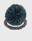 A straw pompom napkin ring in indigo blue color, with a textured center and a twisted rope-like design at the base.