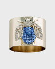A gold-colored napkin ring featuring a blue sparkle bee design.