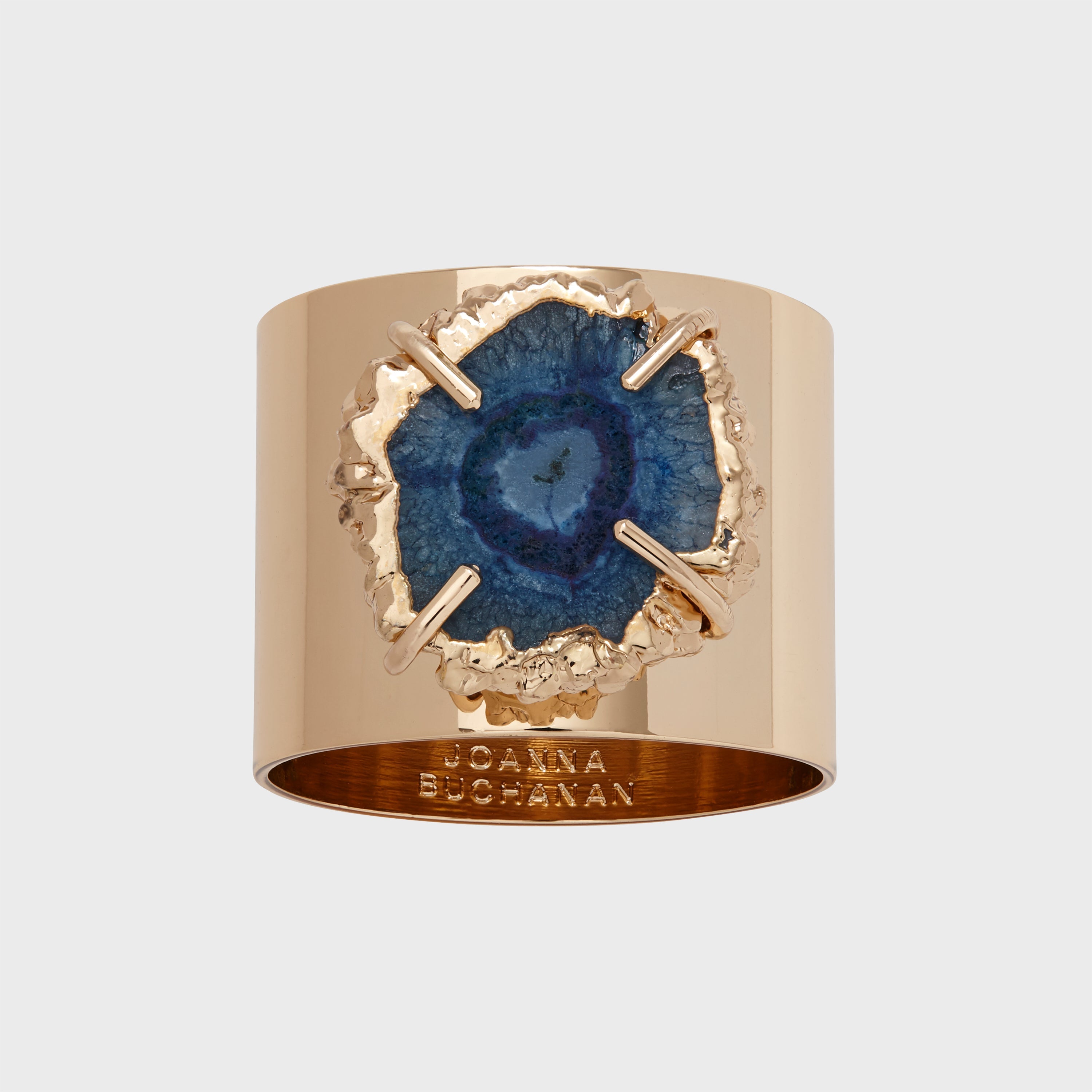 A gold-colored napkin ring featuring a crystal quartz with a blue center