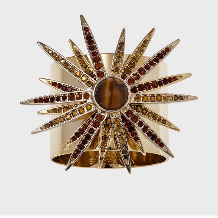 A gold-colored starburst napkin ring featuring a central stone with radiating crystal embellishments.