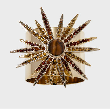 A gold-colored starburst napkin ring featuring a central stone with radiating crystal embellishments.