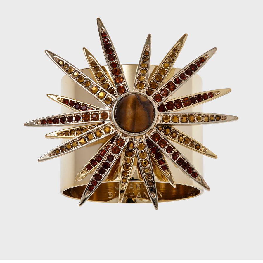 A gold-colored starburst napkin ring featuring a central stone with radiating crystal embellishments.