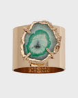 A gold-colored napkin ring featuring a cut of crystal quartz with a seafoam green interior