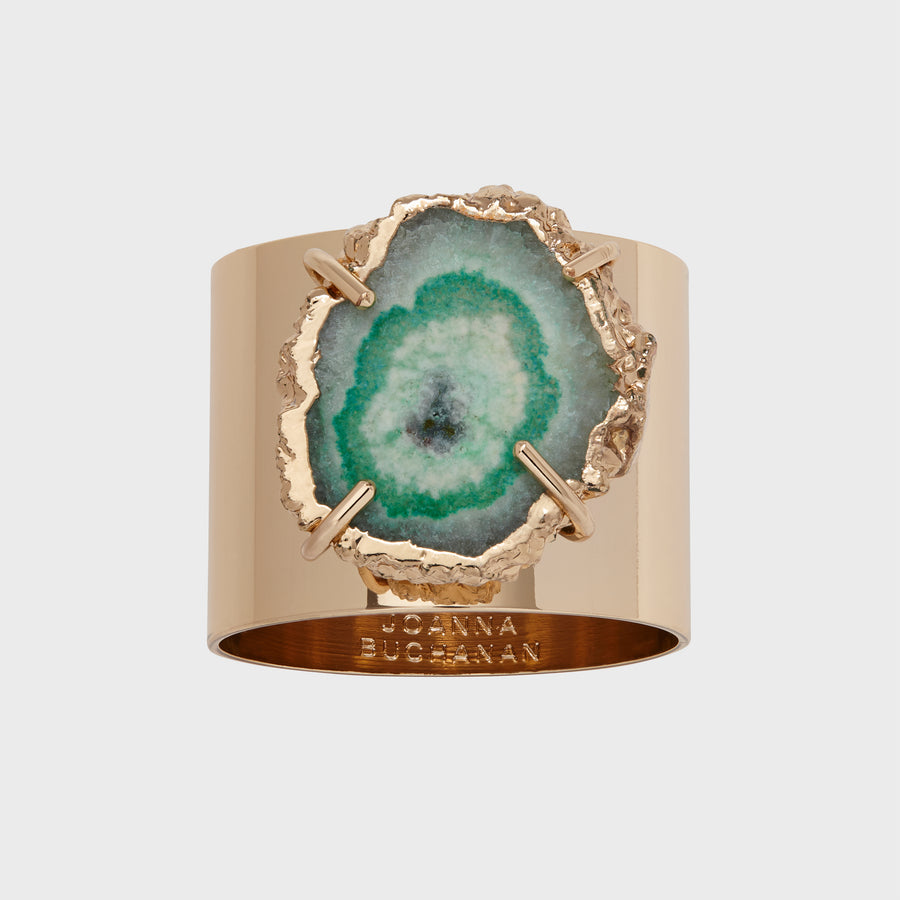 A gold-colored napkin ring featuring a cut of crystal quartz with a seafoam green interior