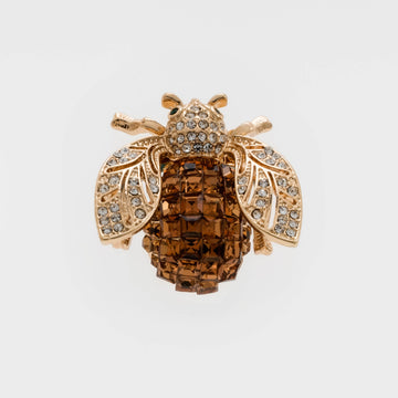 A golden brooch shaped like a bee with a topaz brown body and clear crystal embellishments on its wings and head.