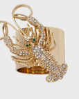 A gold-colored napkin ring featuring a crystal-encrusted lobster design with green accents for eyes.