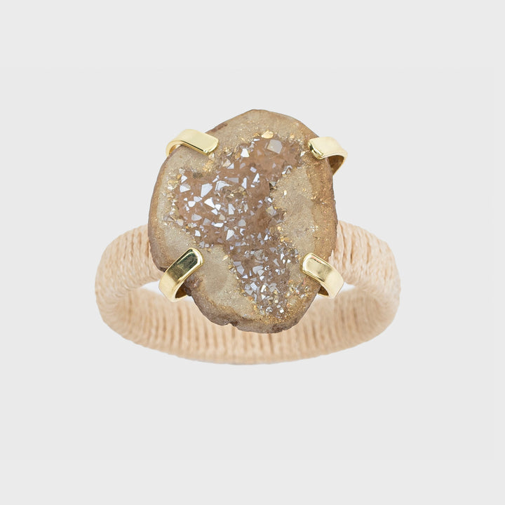 A napkin ring featuring a natural raffia band and a druzy stone centerpiece, with a gold-colored metal clasp.