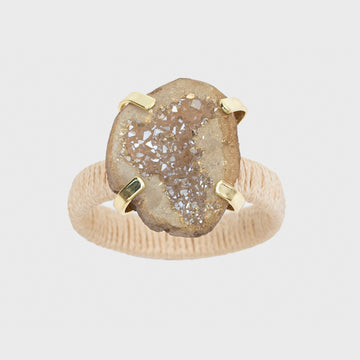 A napkin ring featuring a natural raffia band and a druzy stone centerpiece, with a gold-colored metal clasp.